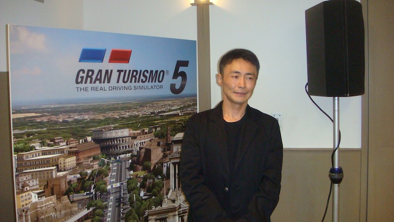 Kazunori Yamauchi, creatore di Gran Turismo, davanti al poster del gioco